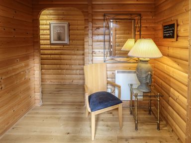 A wooden room with a chair and a glass side table with a lamp along with a wall mirror and a framed picture at The Great Escape in Kenwick near Louth