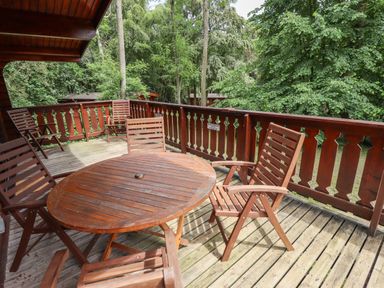 A wooden outdoor deck with a round table and chairs surrounded by trees at The Great Escape in Kenwick near Louth