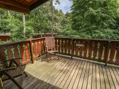 A wooden balcony with two chairs and a wooden railing surrounded by trees at The Great Escape in Kenwick near Louth