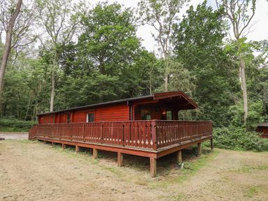A wooden cabin with a wraparound deck surrounded by trees at The Great Escape in Kenwick near Louth