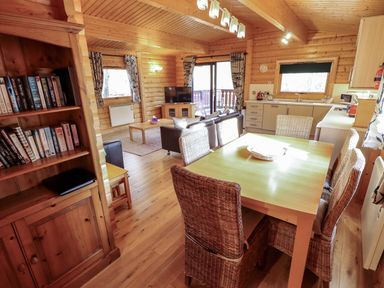 A dining area with wicker chairs and wooden table next to a kitchen with cabinets and a living room with a sofa TV and bookshelf at The Great Escape Kenwick near Louth