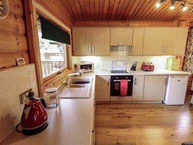 A kitchen with wooden cabinets a red kettle a microwave oven a stove with a red oven mitt and a small refrigerator at The Great Escape in Kenwick near Louth