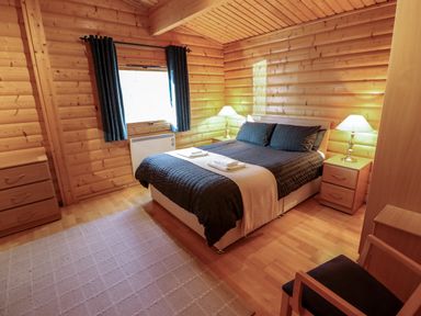 A bedroom with a bed dressed in dark bedding two bedside tables with lamps a window with curtains and wooden furniture at The Great Escape in Kenwick near Louth