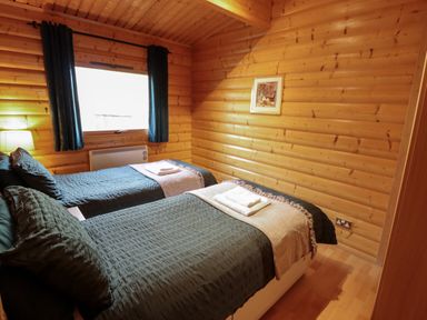 A bedroom with two single beds side by side with dark bedding and towels on top wooden walls and a window with curtains at The Great Escape in Kenwick near Louth