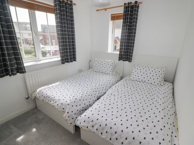 A bedroom with two single beds with white bedding with black triangle patterns and windows with black and white check curtains at 12 Clos Yr Wylan Barry