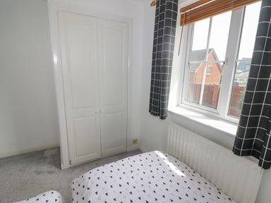 A bedroom with a window and black curtains a radiator a built in white closet and beds with patterned bedding at 12 Clos Yr Wylan Barry