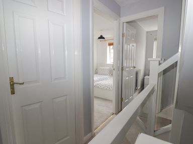A hallway with white doors leading to a bedroom with a bed and a room with a radiator at 12 Clos Yr Wylan in Barry