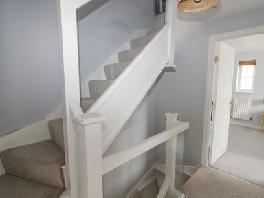 A carpeted staircase with white wooden and glass railing next to a doorway leading to a room with a window at 12 Clos Yr Wylan in Barry
