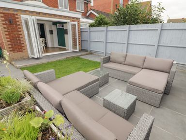 A patio area with outdoor seating and a small grass patch outside a house with open folding doors at 12 Clos Yr Wylan in Barry