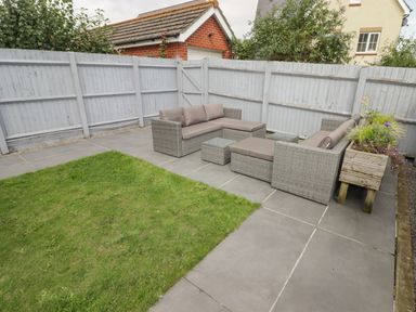 An outdoor patio area with patio furniture and a planter box next to a grass lawn at 12 Clos Yr Wylan in Barry