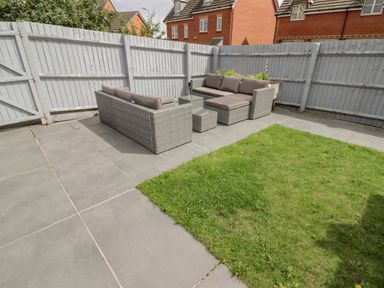 An outdoor patio area with gray cushioned seating and a grass patch at 12 Clos Yr Wylan in Barry