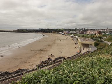 A sandy beach with people walking and buildings along the shore at 12 Clos Yr Wylan in Barry