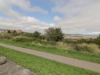 A coastal path with grass and bushes near water with houses in the distance at 12 Clos Yr Wylan in Barry