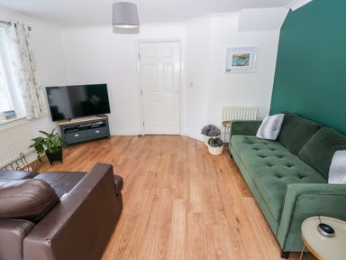 A living room with a green sofa and leather armchair a television on a stand and a wooden floor at 12 Clos Yr Wylan in Barry