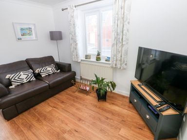 A living room with a brown leather sofa two patterned cushions a floor lamp a window with curtains a plant a tv on a stand and a magazine rack at 12 Clos Yr Wylan in Barry