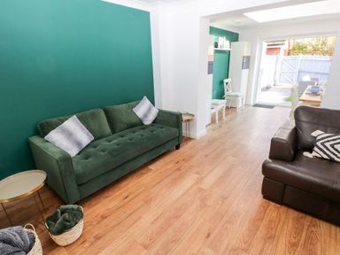 A living room with green and brown sofas and wooden flooring leading to a dining area and garden at 12 Clos Yr Wylan in Barry
