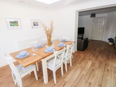 A dining area with a wooden table set for six and white chairs next to a living room in Barry