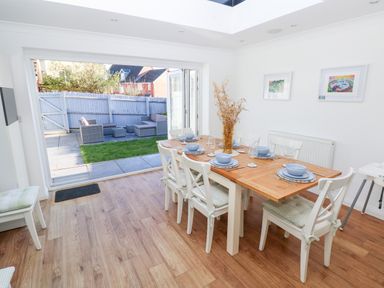 A dining room with a wooden table set for six and chairs with cushions next to a patio and garden at 12 Clos Yr Wylan in Barry