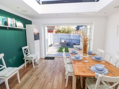 A dining room with a wooden table set for six and chairs next to glass doors opening to a garden at 12 Clos Yr Wylan in Barry