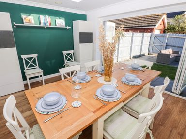 A dining area with a wooden table set for six and chairs opening to a fenced backyard at 12 Clos Yr Wylan in Barry