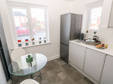 A kitchen area with a glass table and two chairs a refrigerator and a countertop with a kettle and breakfast items at 12 Clos Yr Wylan in Barry
