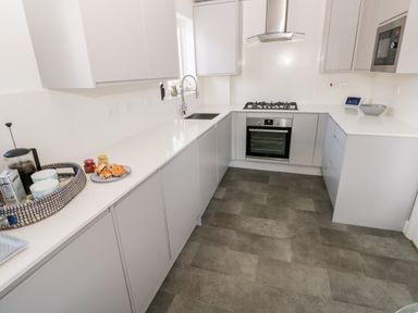A modern kitchen with white countertops gray cabinets a built-in oven a gas stove a stainless steel hood a microwave a sink and a breakfast tray with cups and pastries at 12 Clos Yr Wylan in Barry