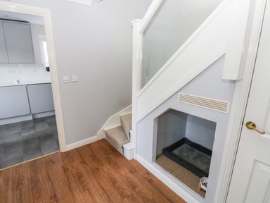 A hallway with wooden floor carpeted stairs and a built-in pet area under the stairs at 12 Clos Yr Wylan in Barry
