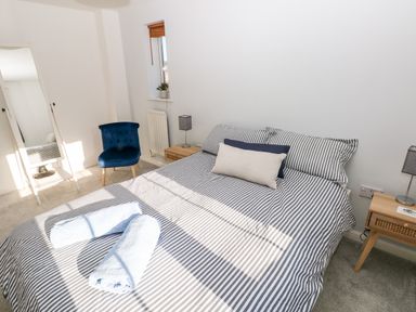 A bedroom with a striped bedspread two rolled towels on the bed a blue chair a full length mirror two bedside tables with lamps and a small window at 12 Clos Yr Wylan in Barry