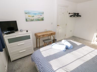 A bedroom with a striped bedspread and towels on the bed a dresser with a TV and clock a wooden desk with a stool and hangers on the wall at 12 Clos Yr Wylan Barry