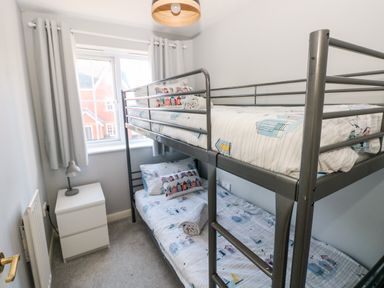 A bedroom with bunk beds, a bedside table with a lamp, and a window with curtains at 12 Clos Yr Wylan in Barry