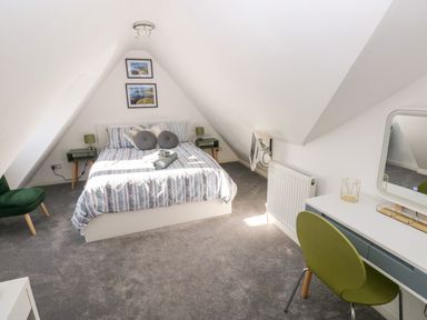 A bedroom with a bed two side tables a green chair a desk with a mirror and a television on the wall at 12 Clos Yr Wylan in Barry