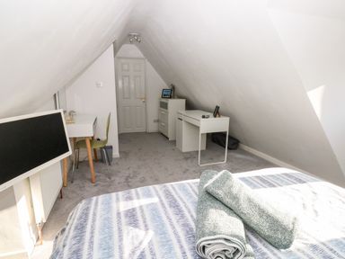 A bedroom with a bed and towels a television a desk with a chair and another desk with drawers at 12 Clos Yr Wylan in Barry