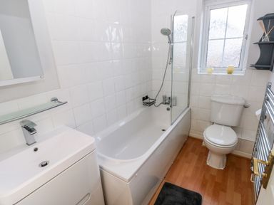 A bathroom with a bathtub shower combination a white sink a toilet a window and a towel rack at 12 Clos Yr Wylan in Barry