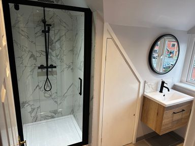 A bathroom with a glass shower enclosure with black fixtures and a wall-mounted sink with a round mirror at 12 Clos Yr Wylan Barry