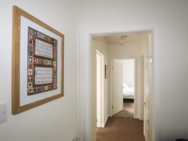 Hallway with framed artwork on the wall and open doors leading to a bedroom at Glan Awel in Nefyn