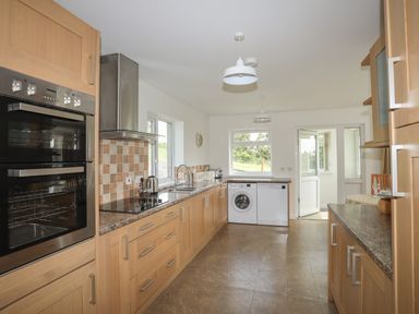 A kitchen with wooden cabinets a double oven a stove a washing machine a dishwasher two windows and a door at Glan Awel in Nefyn