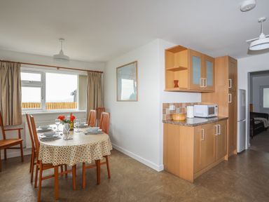 A dining area with a table set for six near a window and a kitchen counter with cabinets and a microwave at Glan Awel in Nefyn