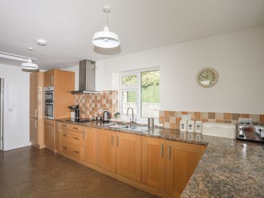 A kitchen with wooden cabinets countertop appliances and a window at Glan Awel in Nefyn