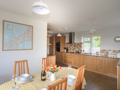 A kitchen with wooden cabinets a dining table with a yellow tablecloth and flowers a map on the wall at Glan Awel in Nefyn