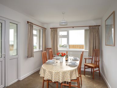 A dining room with a table set for four and windows with curtains at Glan Awel in Nefyn