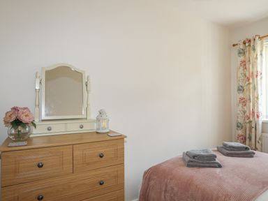 A bedroom with a wooden dresser with a mirror flowers and a lantern next to a bed with folded towels and floral curtains at Glan Awel in Nefyn