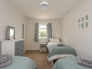 A bedroom with two single beds a dresser a nightstand and a window with floral curtains at Glan Awel in Nefyn