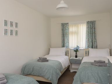 A bedroom with two single beds a bedside table and a window with curtains at Glan Awel in Nefyn