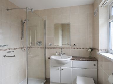 A bathroom with a shower enclosure sink with mirror toilet and window at Glan Awel in Nefyn