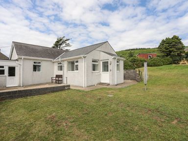 A white house with a grass lawn a rotary clothesline and a bench at Glan Awel in Nefyn