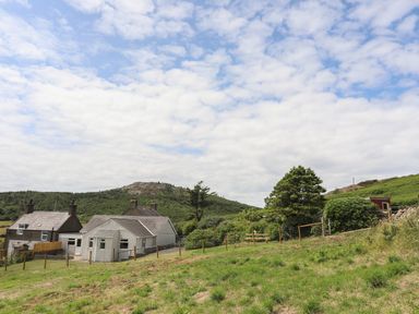 Houses with fenced yard on grassy land with trees and hills under cloudy sky at Glan Awel in Nefyn
