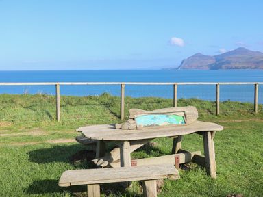 A wooden picnic table and bench on grass with a fence and sea view at Glan Awel in Nefyn