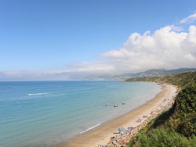 A beach with people on the sand and boats on the water near cliffs at Glan Awel in Nefyn