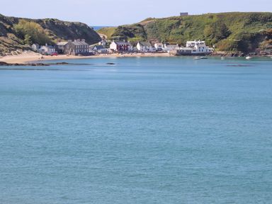 A coastal village with houses along a sandy beach and hills in the background at Glan Awel in Nefyn