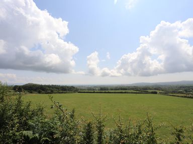 A grassy field with bushes in the foreground and hills in the background at Glan Awel in Nefyn